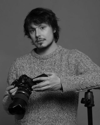Portrait d'un homme qui tient une caméra, avec son coude sur un trépied